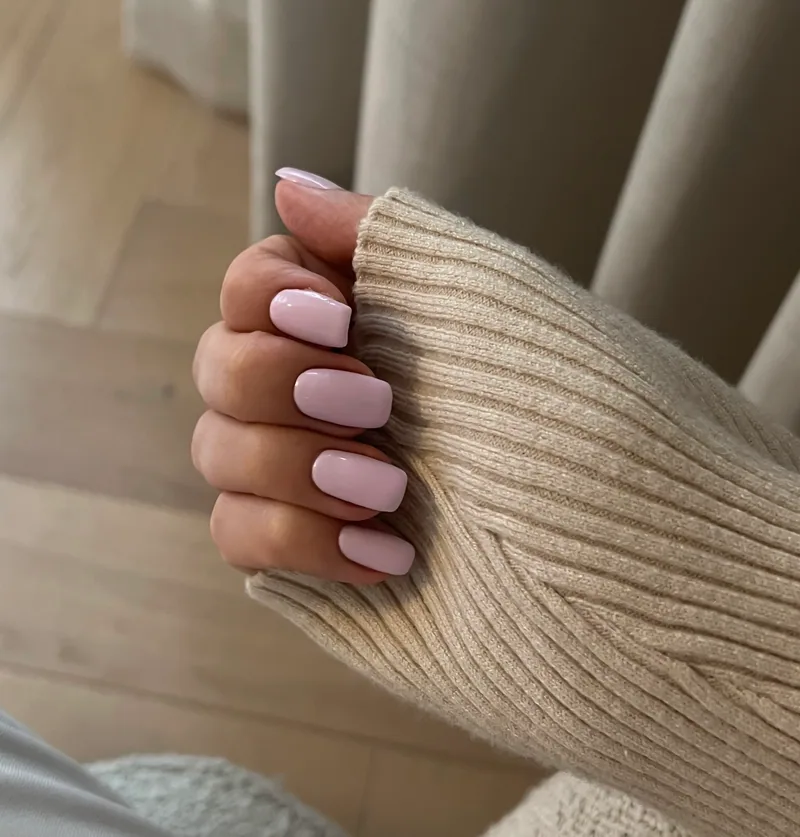 Hånd hvilende på en beige strikkegenser, med negler i lys rosa